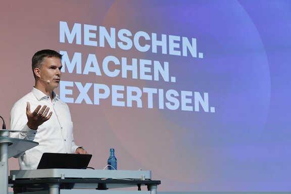 CEO von Holtmann+ Jörg Zeissig erklärt den Dreiklang von Holtmann+ auf der Bühne