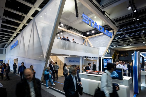 Messestand von Stadler Rail AG, umgesetzt von Holtmann+, in einer Messehalle in Berlin 2024 auf der Messe Innotrans.
